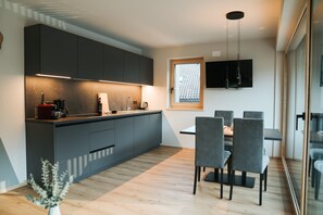 A modern kitchen with dark cabinets, a wooden countertop, and a dining area with grey chairs.