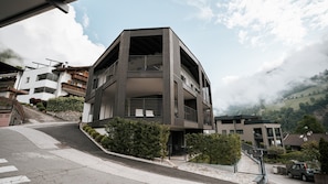 A multi-story building with balconies, a staircase, and a view of a hilly landscape.