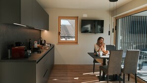 A modern kitchen with a dining area, a TV mounted on the wall, and a window with blinds. - Apartment "Lodge Terrace Exclusive Two" with Mountain View & Wi-Fi (Sankt Martin in Passeier)