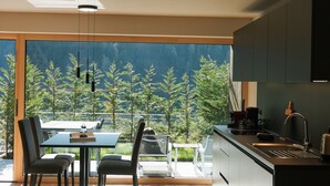 Una cucina moderna con un'ampia finestra, un'area pranzo con tavolo e sedie, e vista sugli alberi.