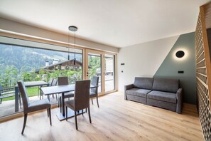 A modern interior with a dining area, sofa, and large windows offering a view of a mountainous landscape.