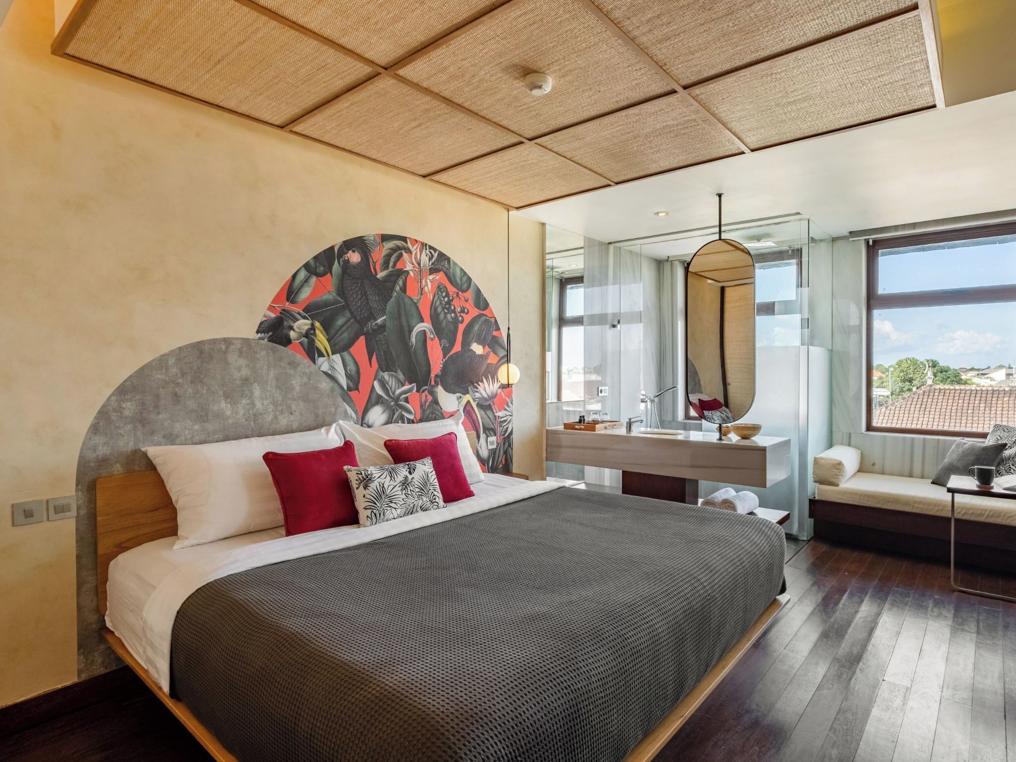 A modern bedroom with a large bed, a round mirror, a vanity with a sink, and a view of the city through large windows.
