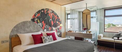 A modern bedroom with a large bed, a round mirror, a vanity with a sink, and a view of the city through large windows.
