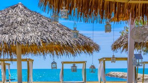 Un paisaje playero con sombrillas de paja, faroles colgantes y sillones blancos para relajarse.
