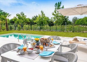A poolside breakfast setup with a table, chairs, and a dining area overlooking a swimming pool. - Pareus Beach Resort (Caorle)