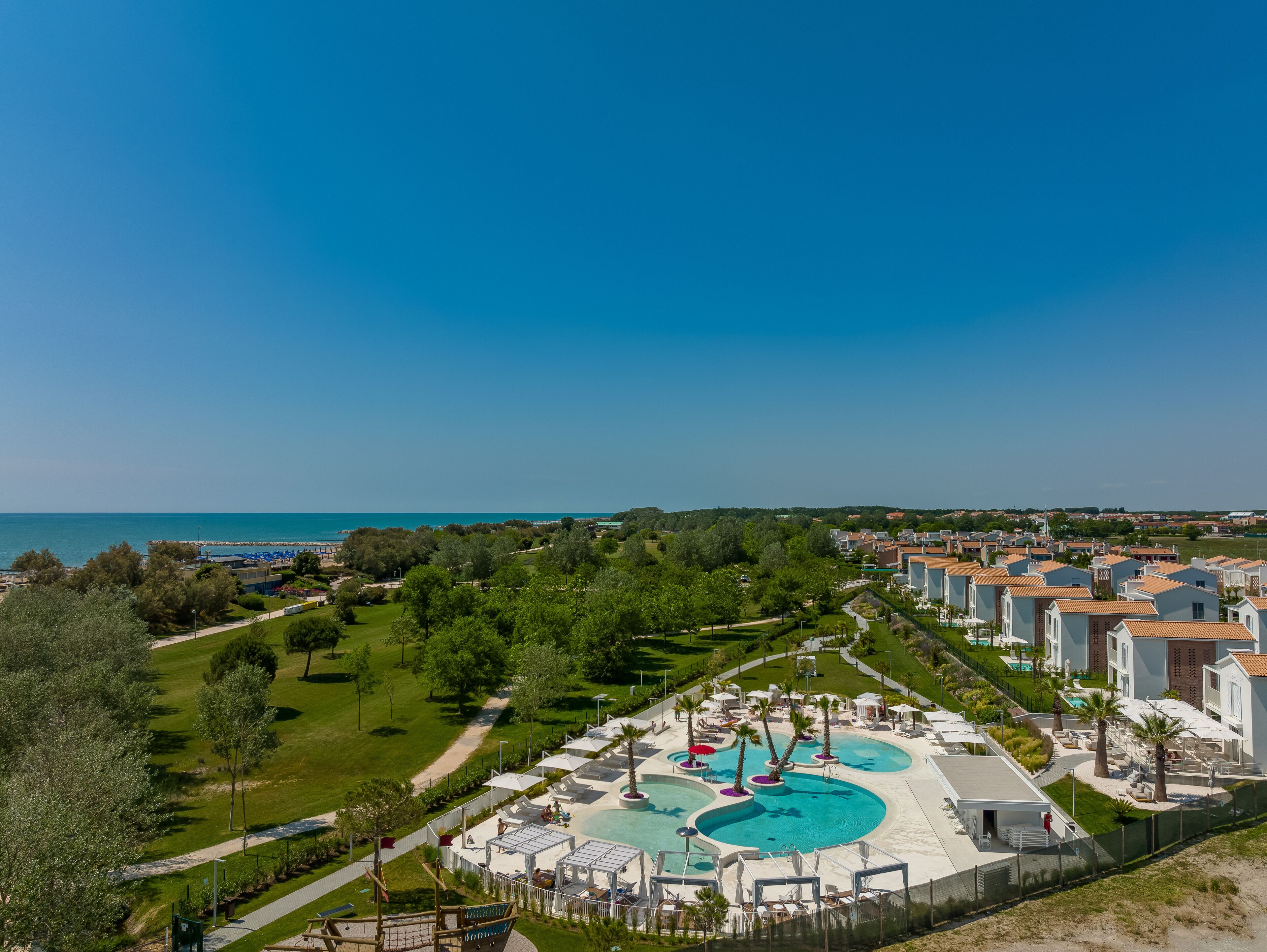 A resort with a central swimming pool, multiple lounge areas, and a view of the sea.