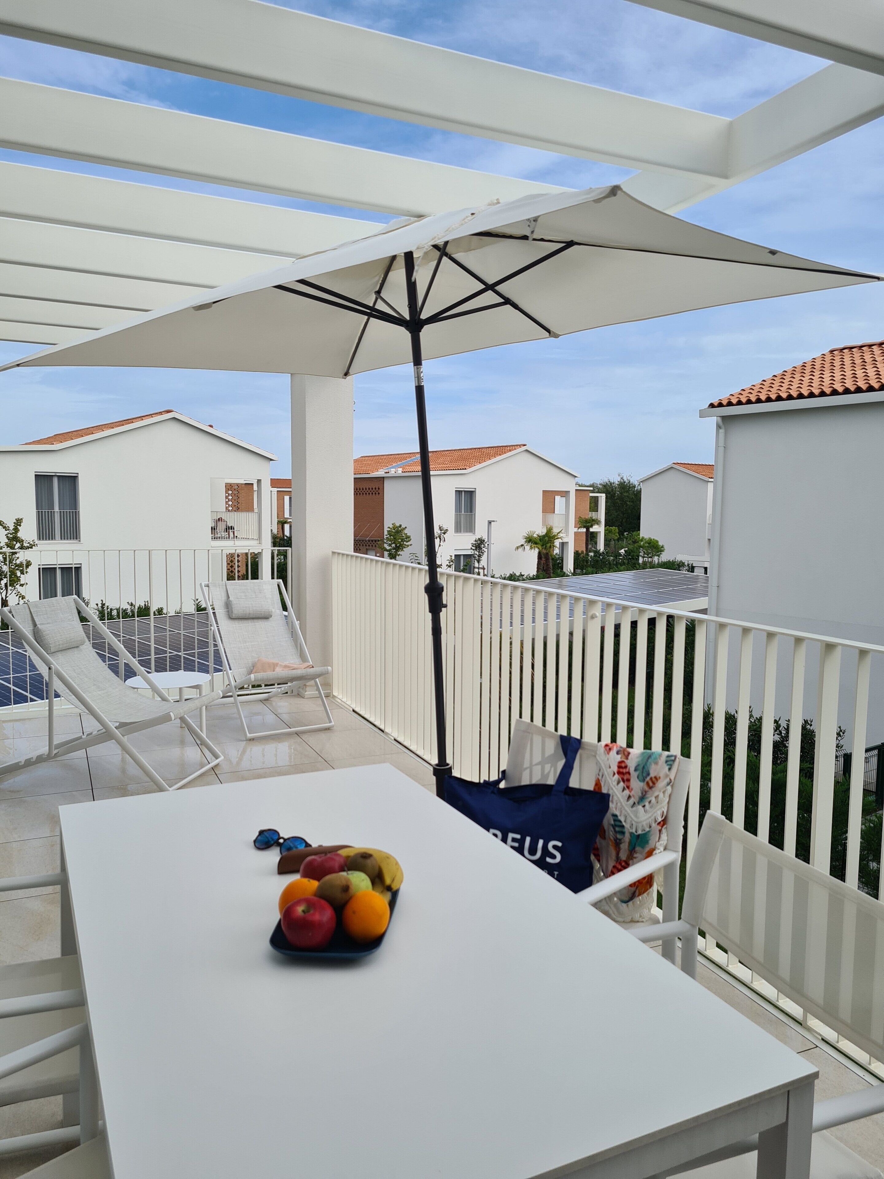 A terrace with a white table, a fruit bowl, and a blue bag.