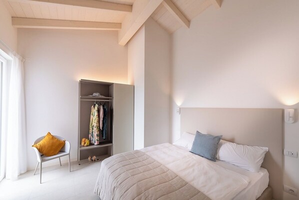 A bedroom with a bed, a wardrobe, a chair, and a nightstand. - Pareus Beach Resort (Caorle)