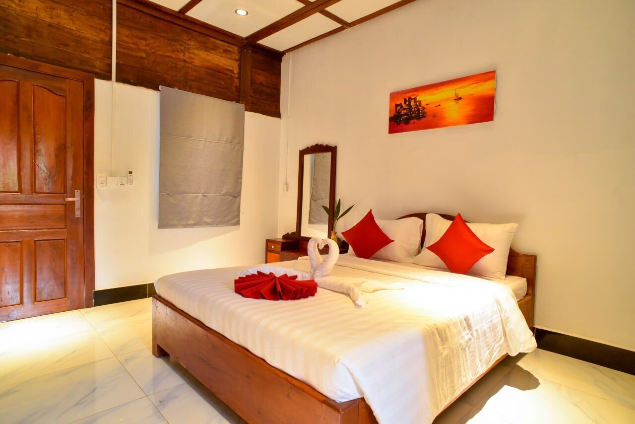 A hotel room with a wooden bed frame, white bedding, and a red pillow.