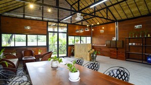 Un espacio interior amplio con una mesa de madera, sillas de mimbre y plantas en macetas.