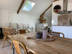 Un coin repas avec une table et des chaises en bois, un plafond de style industriel avec une lucarne, un canapé et un buffet rustique.