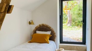 Un dormitorio con cama, un taburete pequeño, una ventana y estructura de vigas de madera.