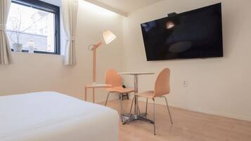 Habitación de hotel con cama, televisión montada en la pared, una mesita con dos sillas y una ventana con cortinas.