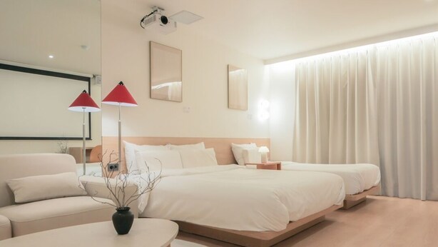Moderni hotellihuone, jossa on suuri sänky, yöpöytä, punainen lamppu, peili ja ikkuna, jossa on verhot.