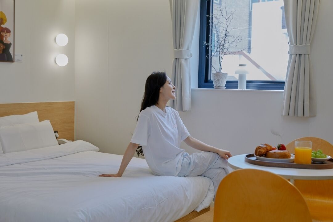 A hotel room with a bed, a dining table with breakfast, and a window with curtains.