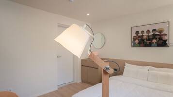 Una habitación de hotel con cama, mesita de noche, lámpara, un cuadro en la pared y una puerta.