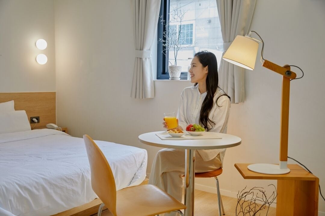 A hotel room with a bed, a dining table with breakfast, a lamp, and a window with curtains.