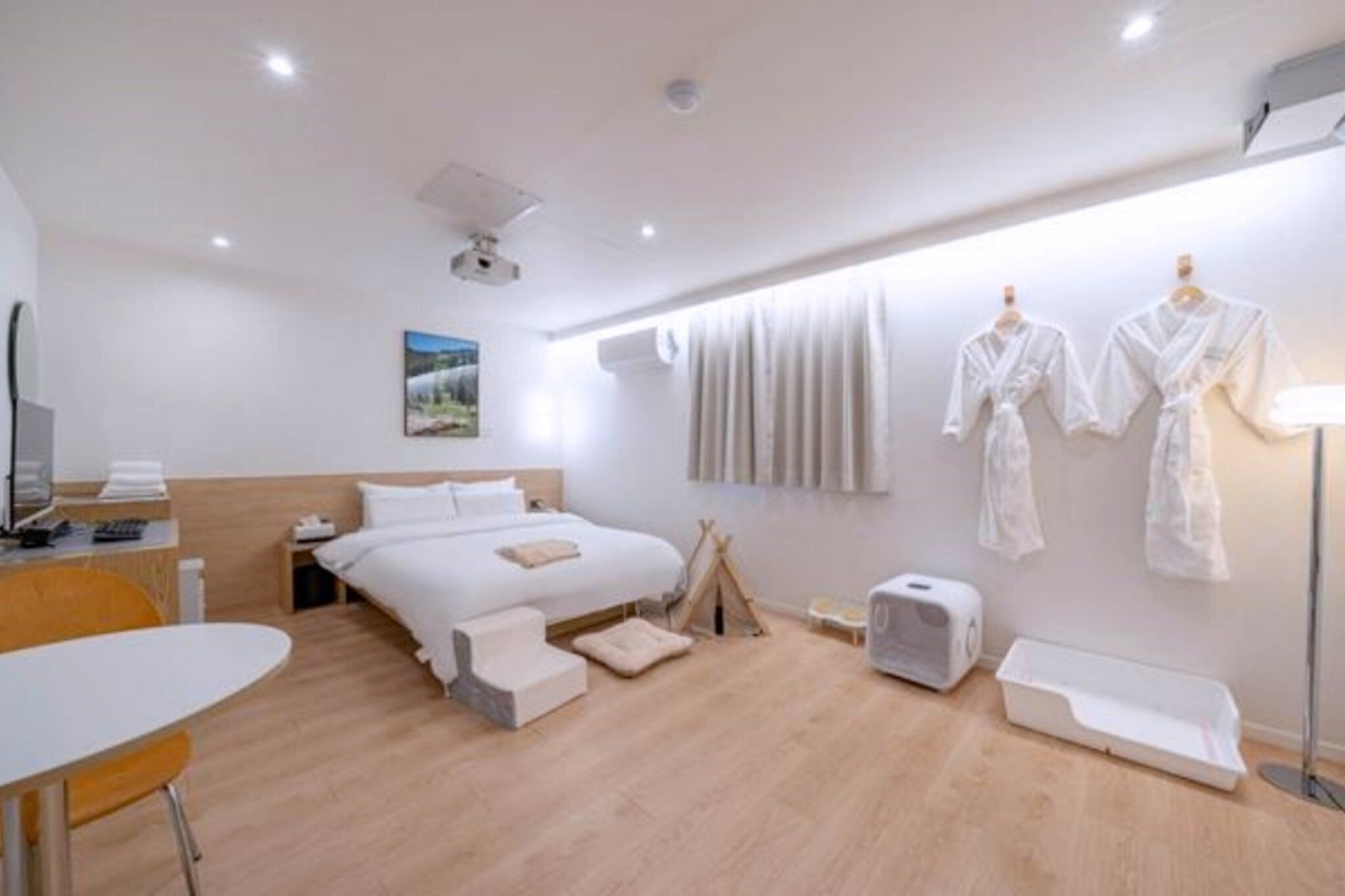 A modern hotel room with a bed, bedside table, chair, and a window with curtains.