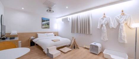 A modern hotel room with a bed, bedside table, chair, and a window with curtains.