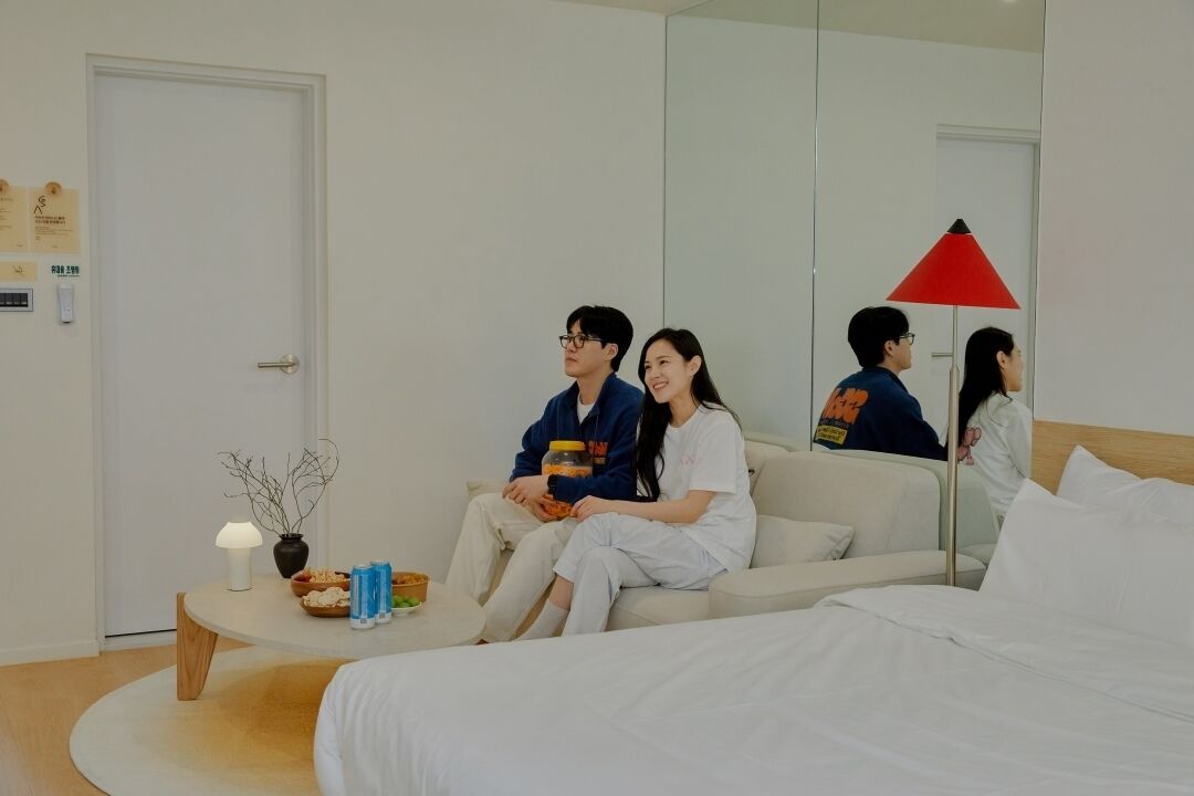 A hotel room with a bed, a sofa, a small table with snacks, and a red lamp.