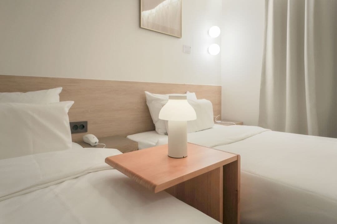 A hotel room with a wooden headboard, a bedside table with a lamp, and a nightstand with a phone.