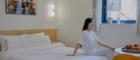Una habitación de hotel con una cama, una mesa redonda con un plato de comida, una ventana con cortinas y una lámpara fijada a la pared.