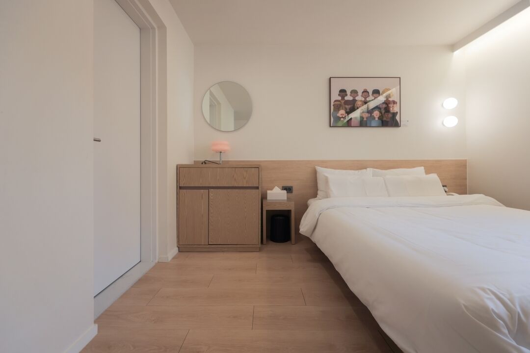 Une chambre à coucher comprenant un lit, une table de chevet, une commode, un miroir et un tableau accroché au mur.