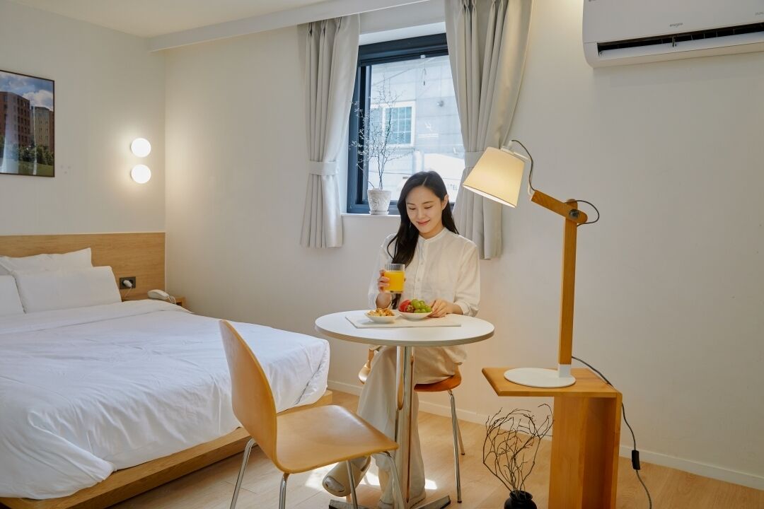 A hotel room with a bed, a round table with a lamp, and a window with curtains.