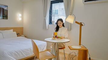 A hotel room with a bed, a round table with a lamp, and a window with curtains.