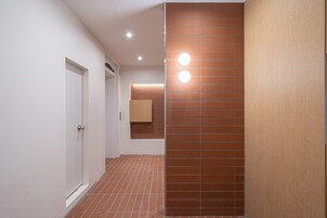 Un pasillo con una puerta blanca, pared con baldosas marrones y luces empotradas en el techo.