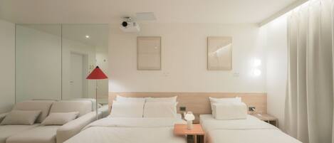 Habitación de hotel con dos camas, un sofá, una mesita de noche con lámpara y un espejo grande.