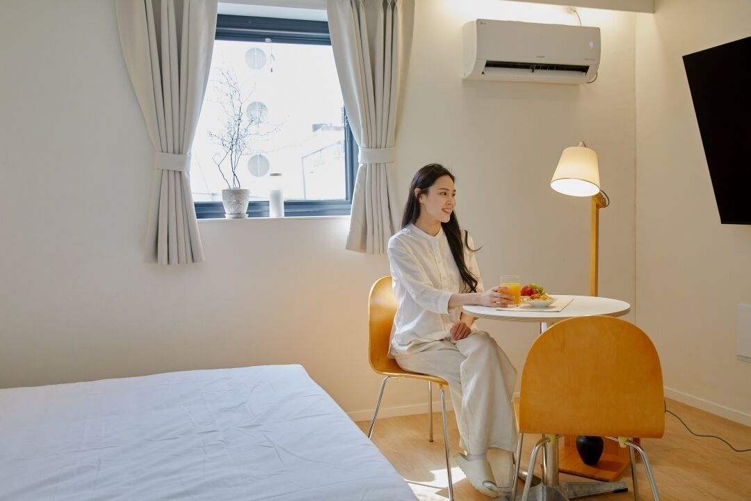 Une chambre d’hôtel avec un lit, une table à manger avec une lampe et une fenêtre avec des rideaux.