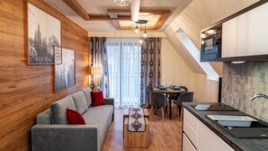 A modern living room with a sofa, coffee table, and dining area. A kitchen with a microwave and sink is visible. - Sun & Snow Resorts G Białka Tatrzanska (Bukowina Tatrzanska)
