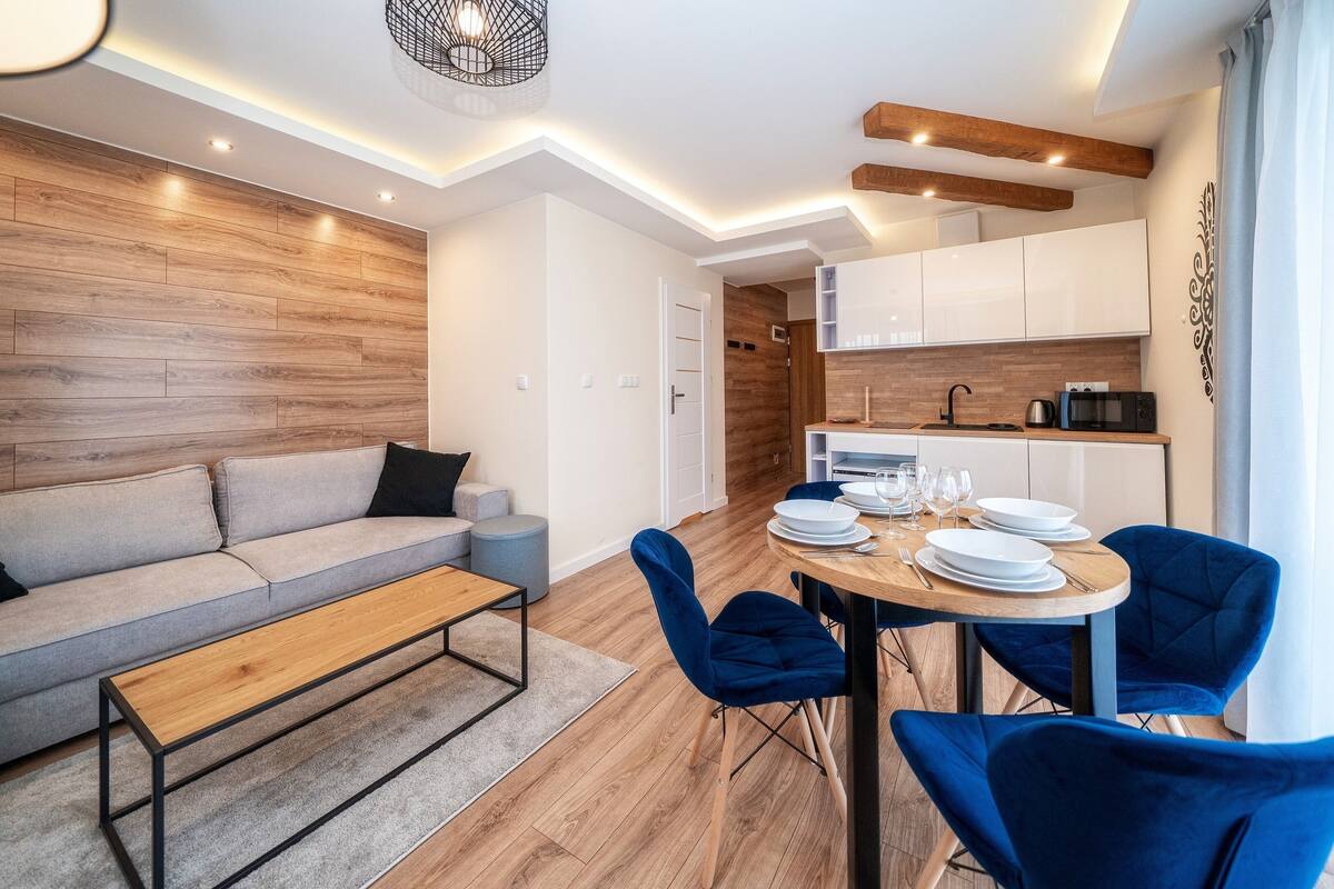Uma sala de estar moderna com um sofá, uma mesa de centro e uma área de jantar com uma mesa redonda e cadeiras azuis.
