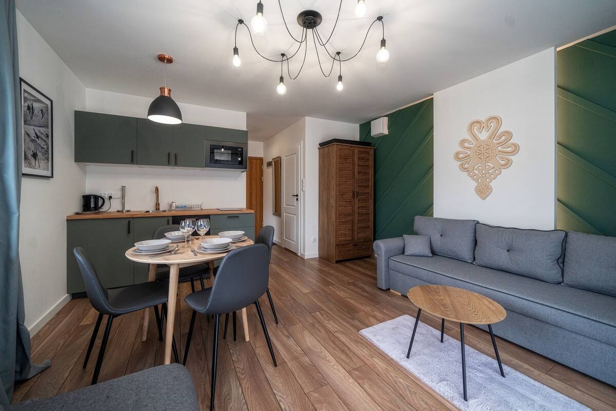 Uma sala de estar moderna com um sofá cinzento, uma mesa de centro de madeira e uma área de jantar com uma mesa redonda e cadeiras.
