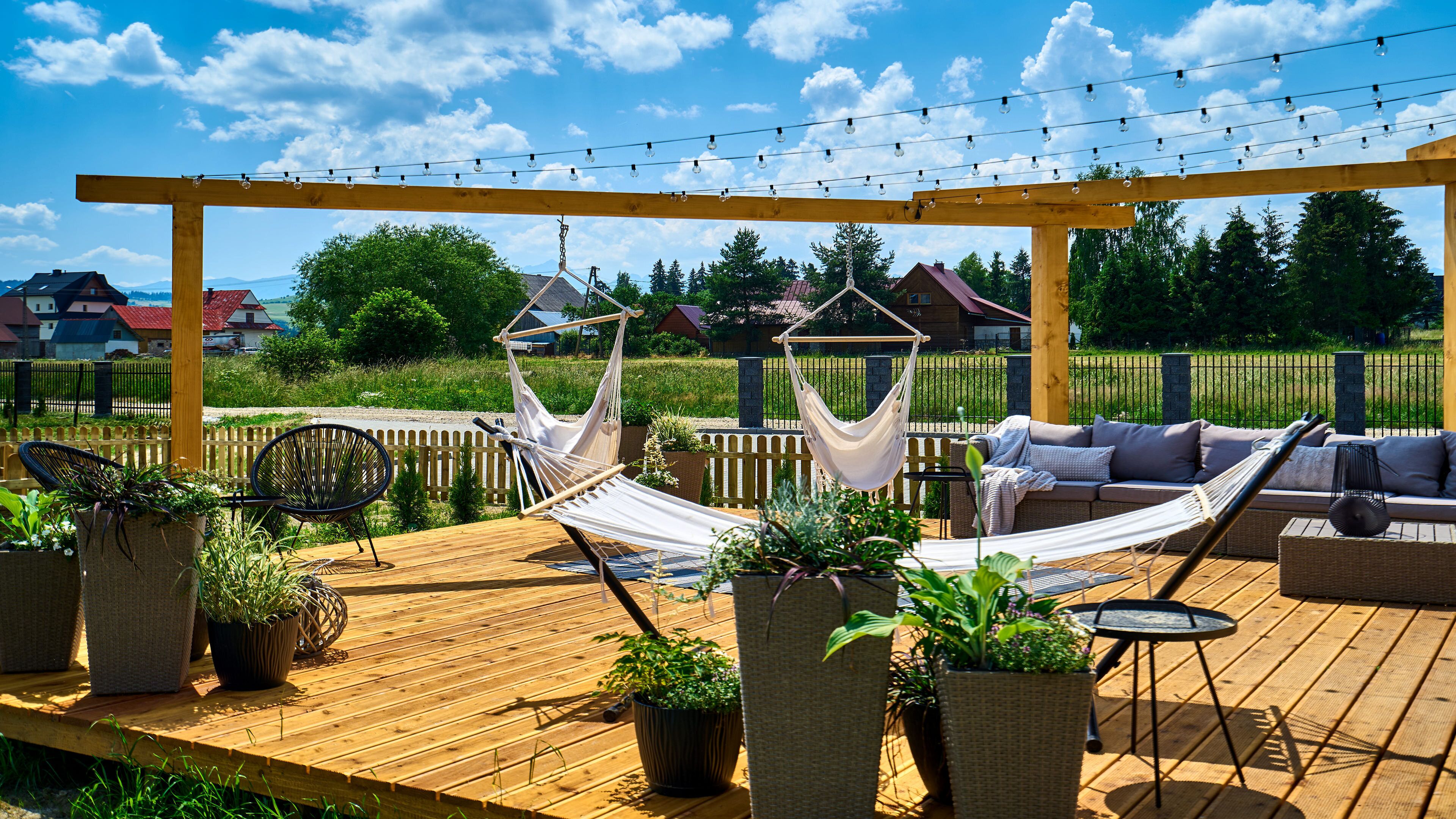 A wooden deck with a hammock, a sofa, and potted plants.