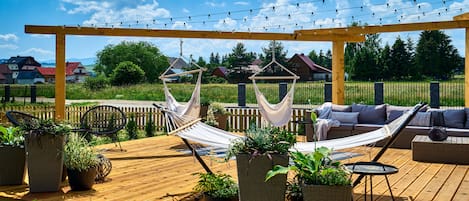 A wooden deck with a hammock, a sofa, and potted plants.