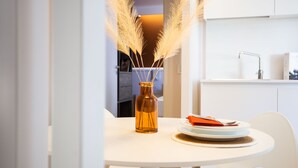 A white dining table with a vase of pampas grass, a plate with a red napkin, and a white chair. - The Lady C - High Apartments (Tropea)
