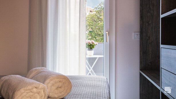 A room with a bed, a window with curtains, a view of a balcony with a table and flowers, and a wooden cabinet. - The Lady C - High Apartments (Tropea)