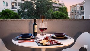 A table set with a bottle of wine, two glasses of red wine, a bowl of cheese, and a plate of cured meats on a balcony overlooking a cityscape. - The Lady C - High Apartments (Tropea)