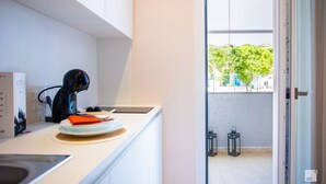 A modern kitchen with white cabinets, a coffee machine, and a view of the outside through a glass door. - The Lady C - High Apartments (Tropea)