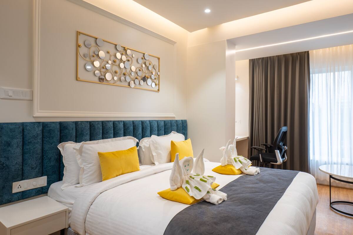 A hotel room with a large bed, a headboard, a wall art piece, a desk, and a chair.