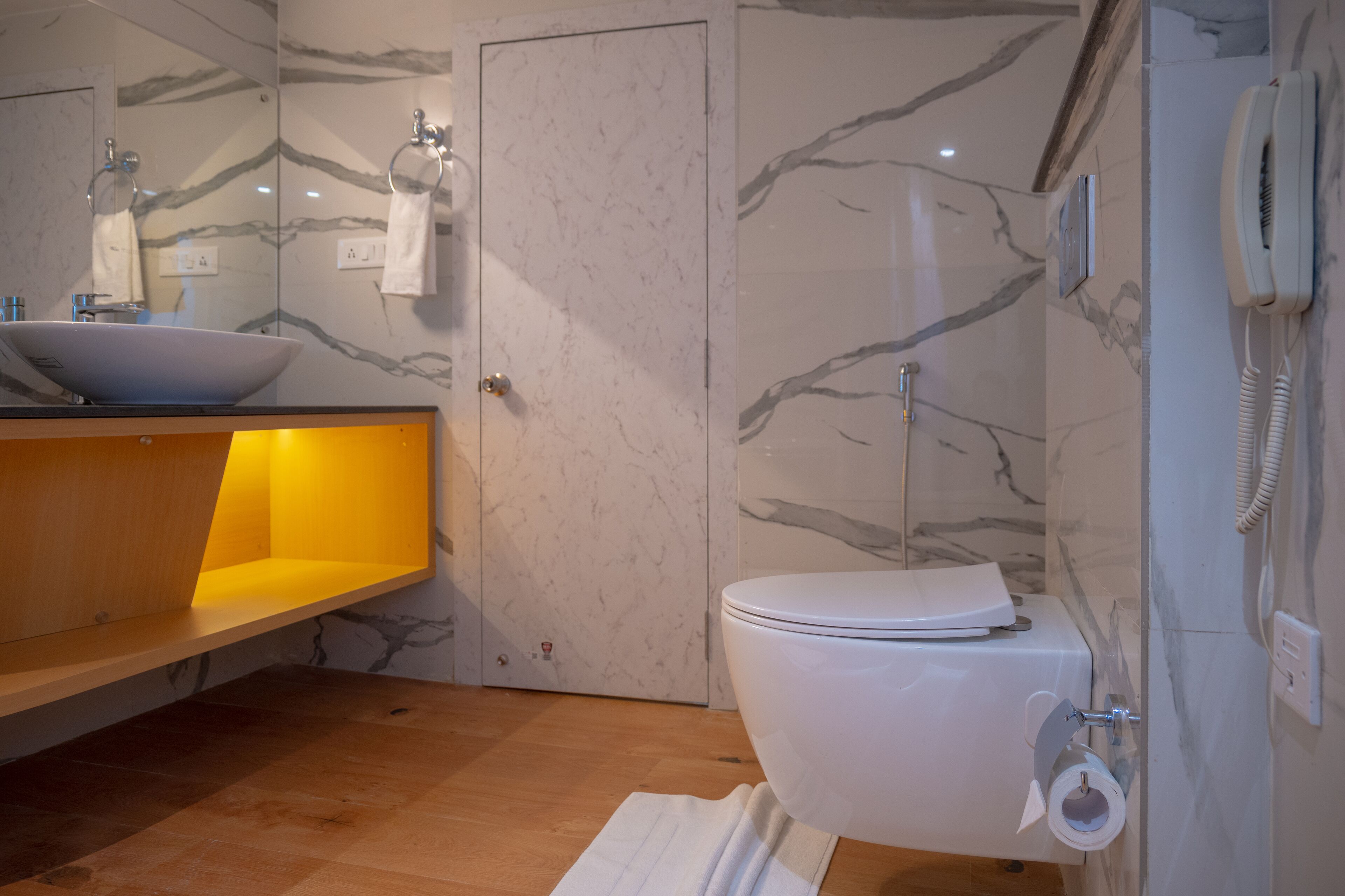 A bathroom with a marble wall, a white toilet, a sink with a mirror, and a telephone.