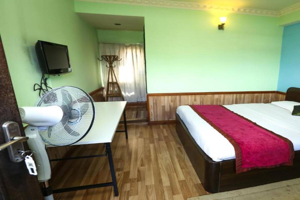 Una habitación de hotel con cama, mesita de noche, ventilador y televisión en la pared.