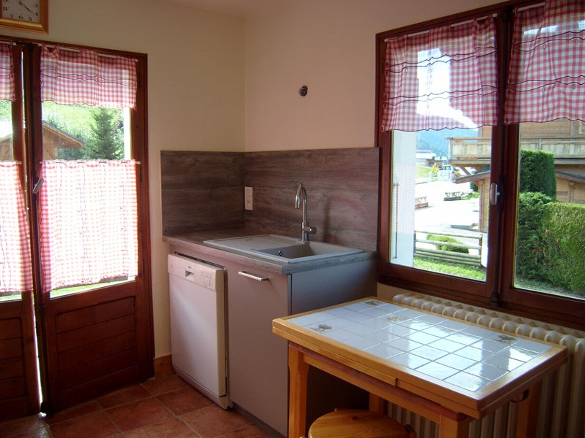A compact kitchen with a sink, a dishwasher, and a small table with a tiled top.