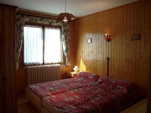A wooden-paneled room with a bed, a window with curtains, a lamp, and a radiator. - Chalet for 8 at the foot of the slopes with parking 50m from lifts (Crest-Voland)