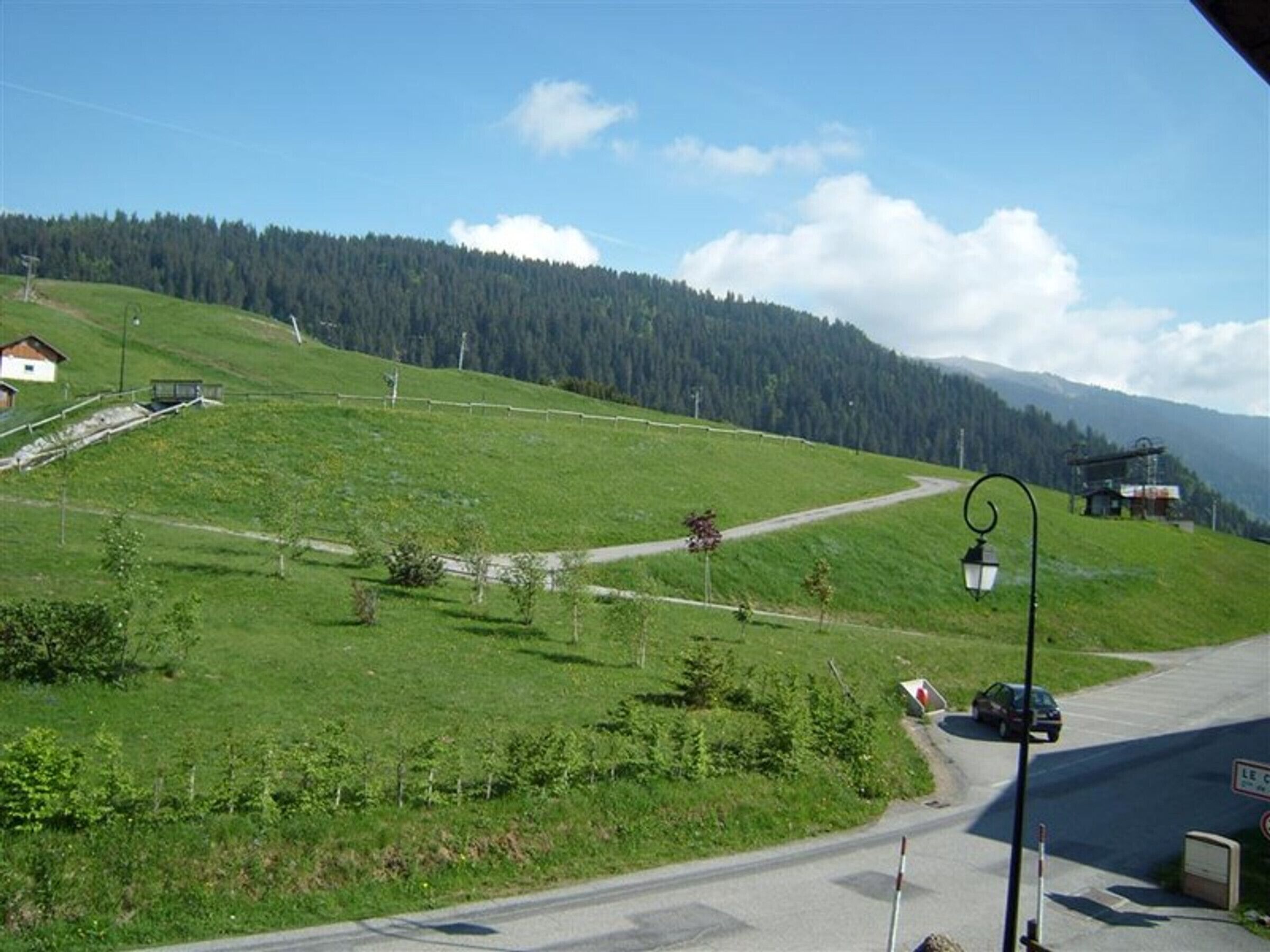 Eine ländliche Straße schlängelt sich durch eine grüne Landschaft, mit einem kleinen Gebäude und einem geparkten Auto am Rand.
