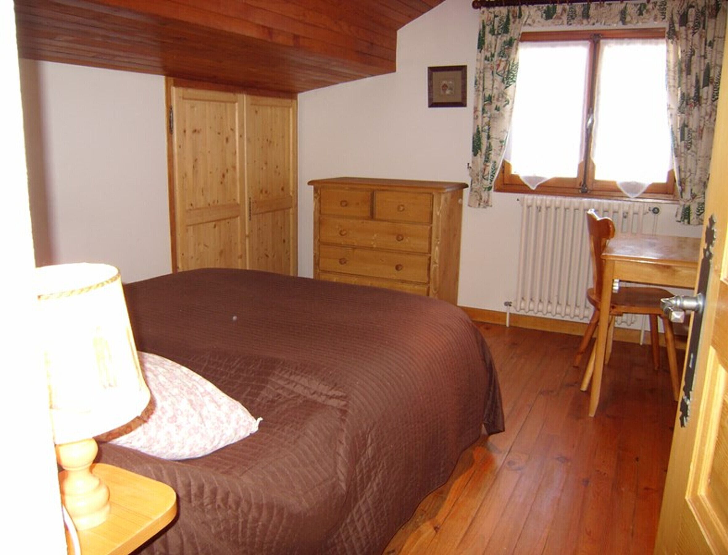 Une chambre à coucher avec un lit en bois, une commode en bois, un bureau en bois et une fenêtre avec des rideaux.