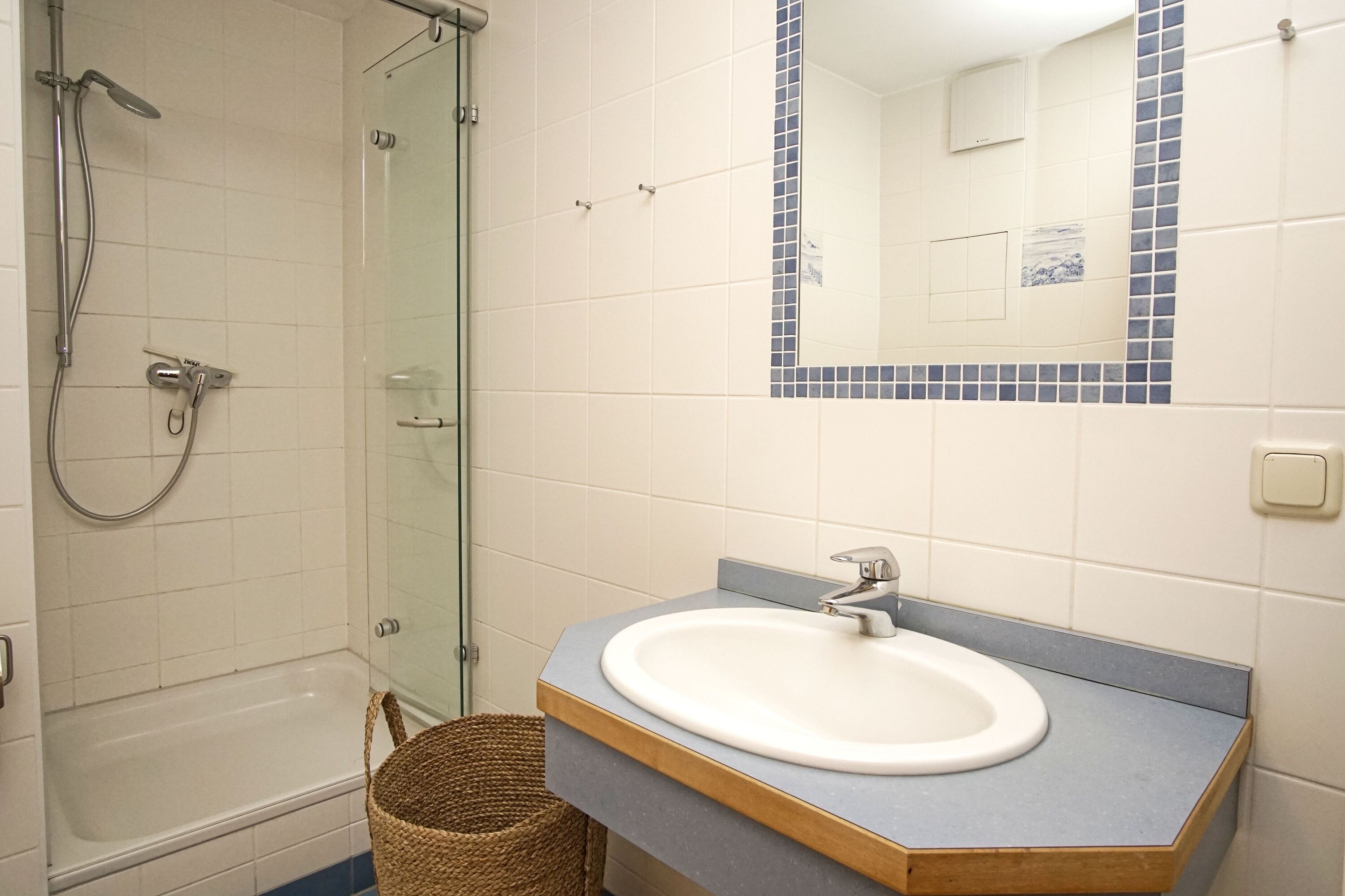 A bathroom with a glass shower enclosure, a bathtub, a sink with a mirror above it, and a small wicker basket.