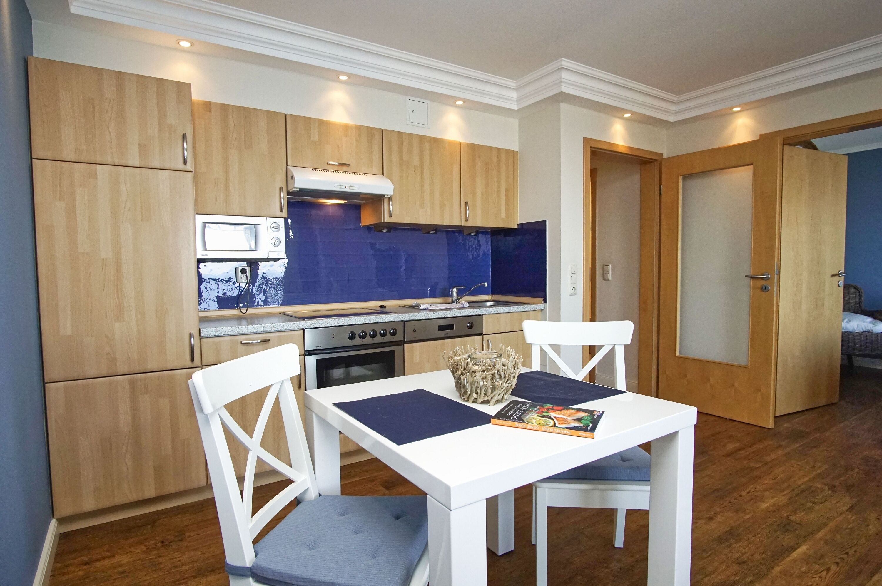 Une cuisine compacte avec des meubles en bois, un four à micro-ondes et une cuisinière. On y trouve une table à manger avec deux chaises et un bol décoratif.